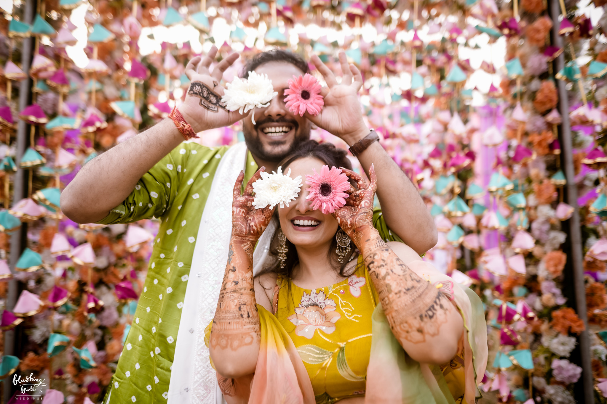 Couple holding flowers up to their eyes at the mehendi