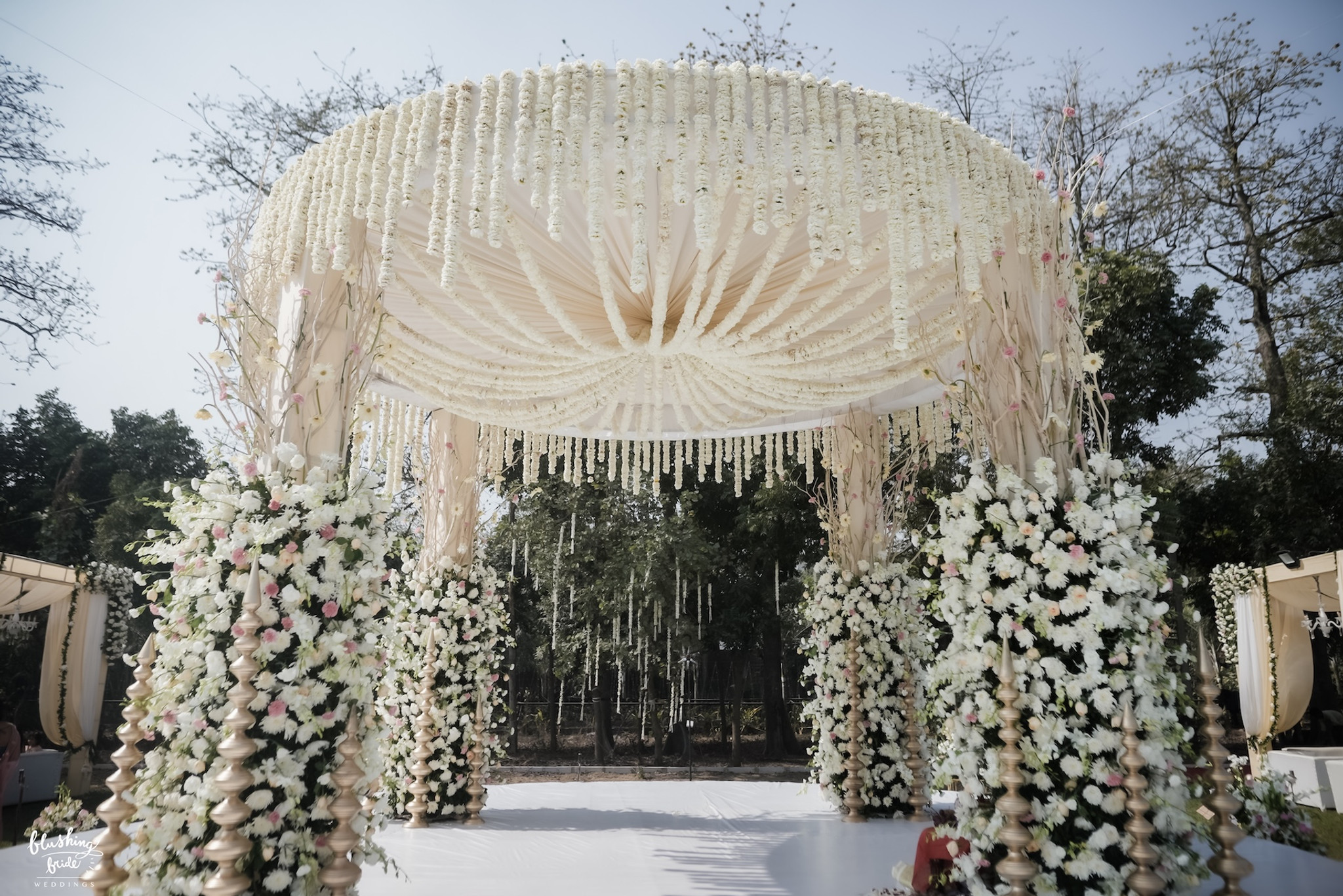 Open-air mandap under a floral chandelier canopy in daylight